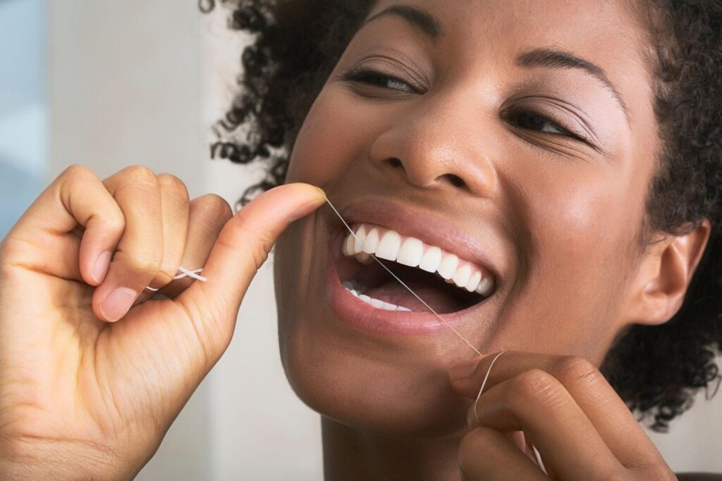 woman flossing her teeth while smiling