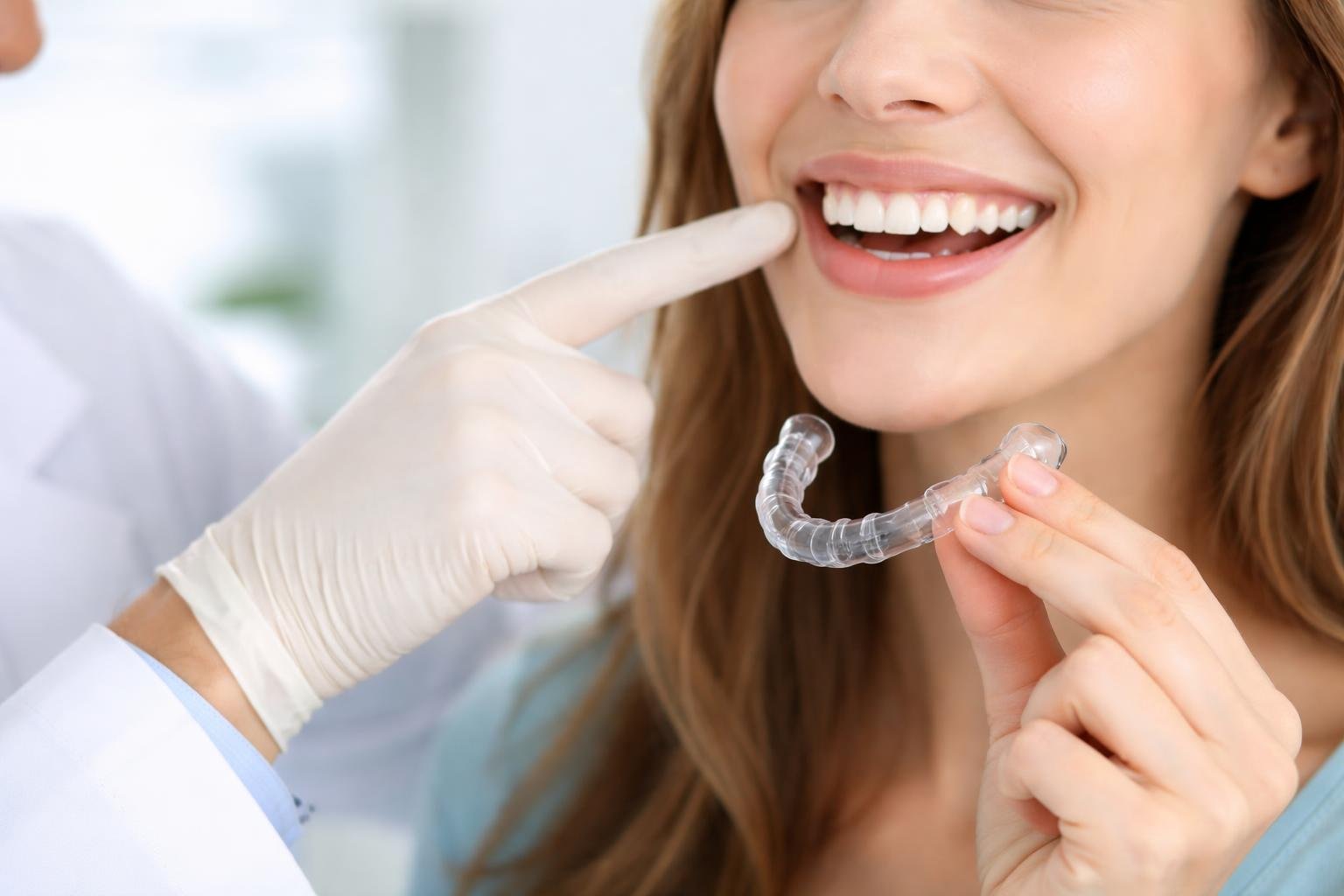 Dentist showing a patient how an Invisalign clear aligner fits over their teeth in a dental clinic.