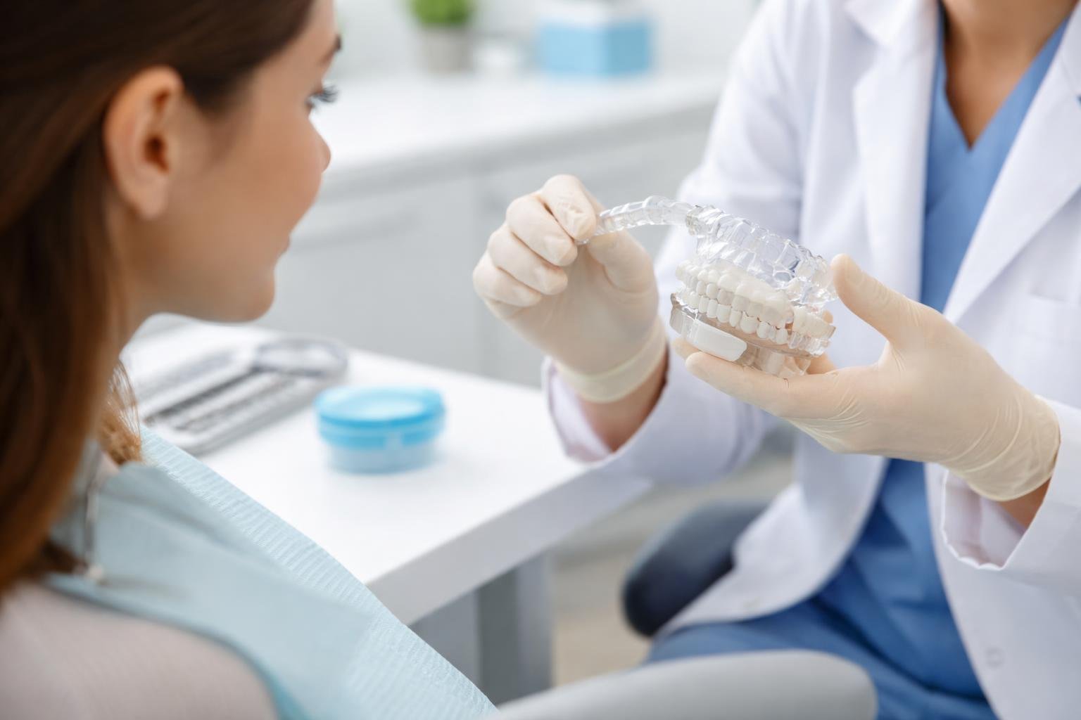 A dental professional shows a clear Invisalign retainer to a patient in a modern dental office.