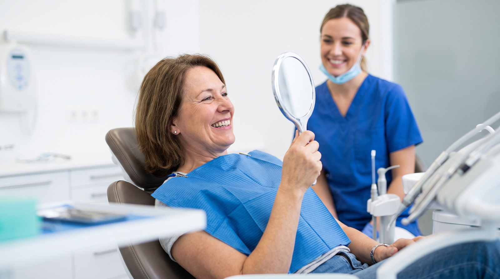 Patient admiring a restored confident smile in a mirror after tooth replacement