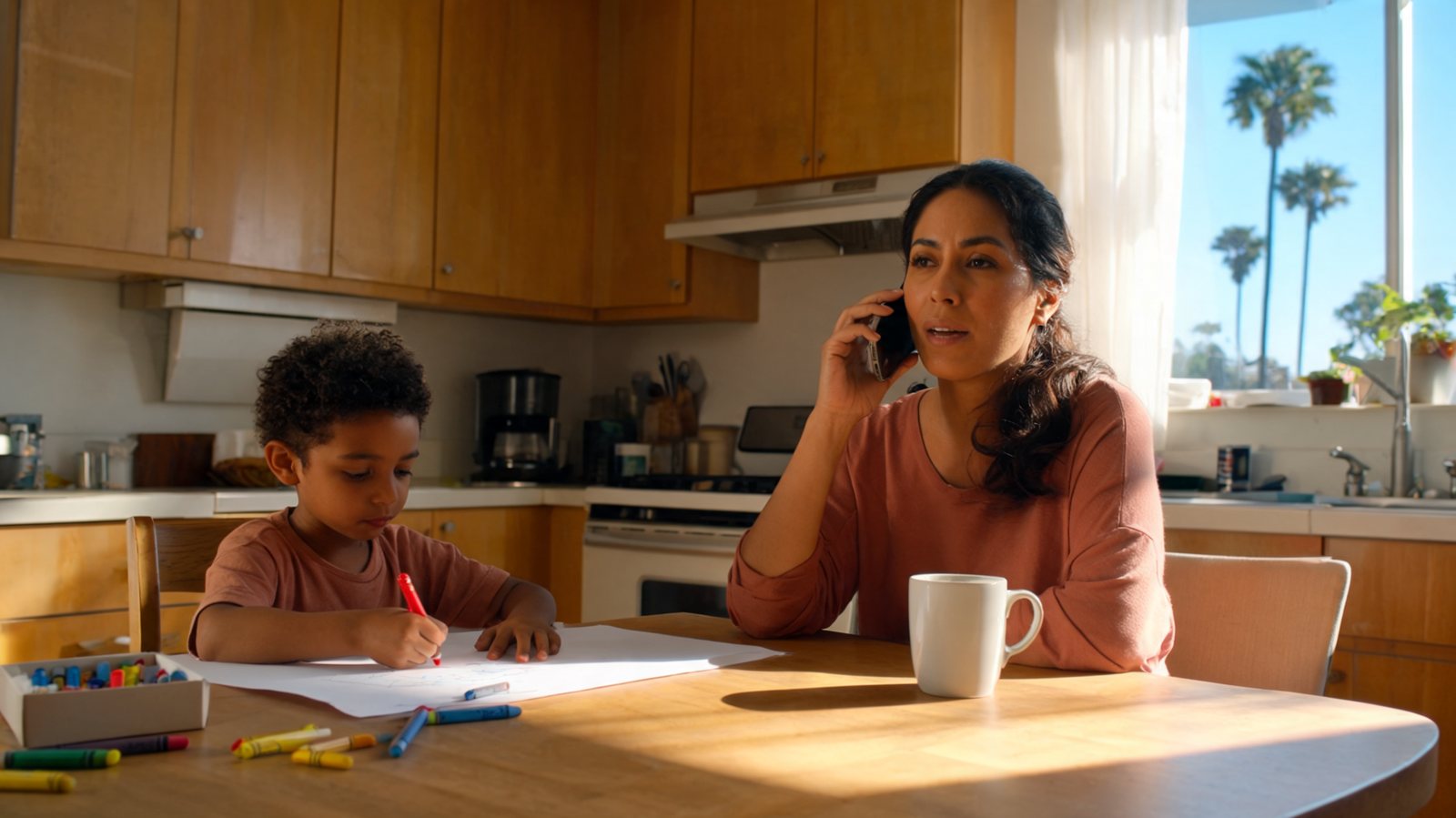 Mother calling to book a Medi-Cal dental appointment while her son draws at the kitchen table